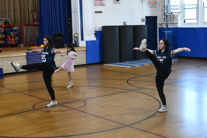 A group of young dancers in school uniforms perform a dance routine on a gymnasium floor, showcasing energetic movements and teamwork.