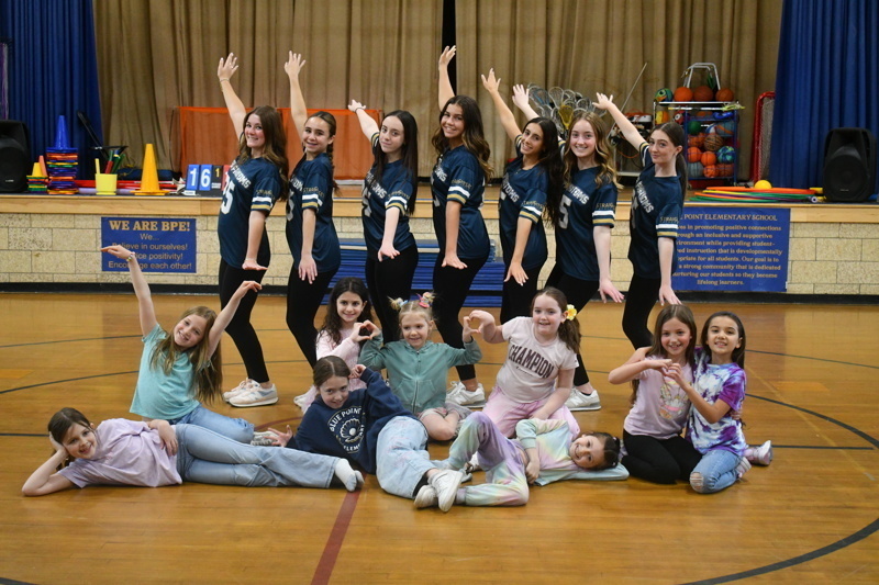 Group of cheerleaders and young dancers posing together on a gymnasium floor, showcasing their teamwork and enthusiasm during a performance at Point Elementary School.