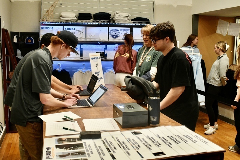 Interior view of Long Island Sign Designs showcasing a variety of custom apparel, including hoodies and printed designs, along with promotional pricing.