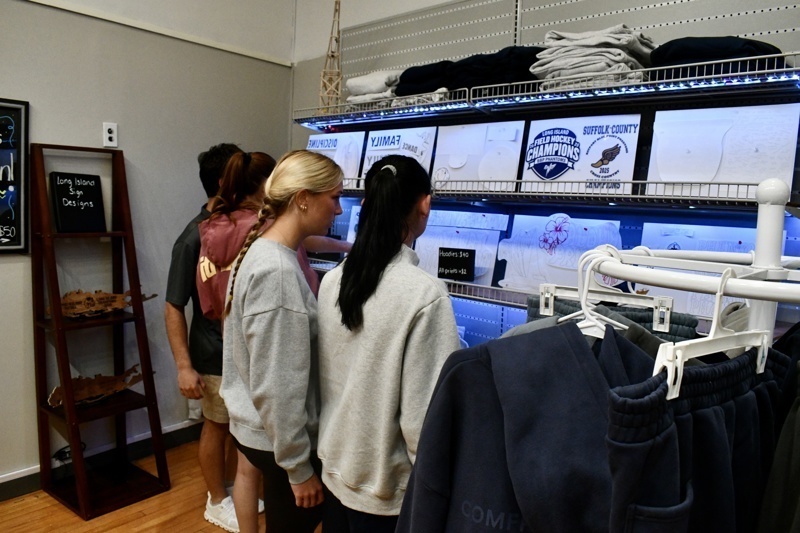 Interior view of Long Island Sign Designs showcasing a variety of custom apparel, including hoodies and printed designs, along with promotional pricing.