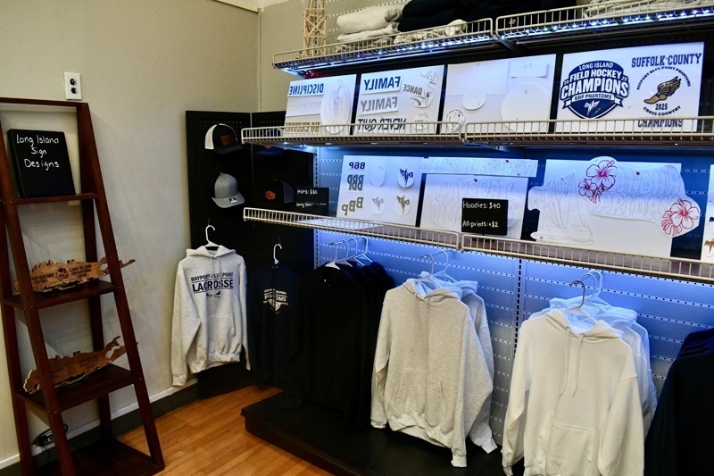 Interior view of Long Island Sign Designs showcasing a variety of custom apparel, including hoodies and printed designs, along with promotional pricing.
