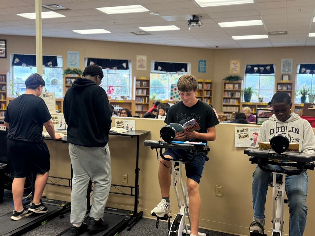 Students reading while working out in the library on reading bikes and walking pads