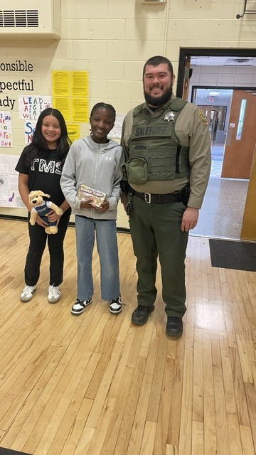 Two students pose for a picture with a police officer. 