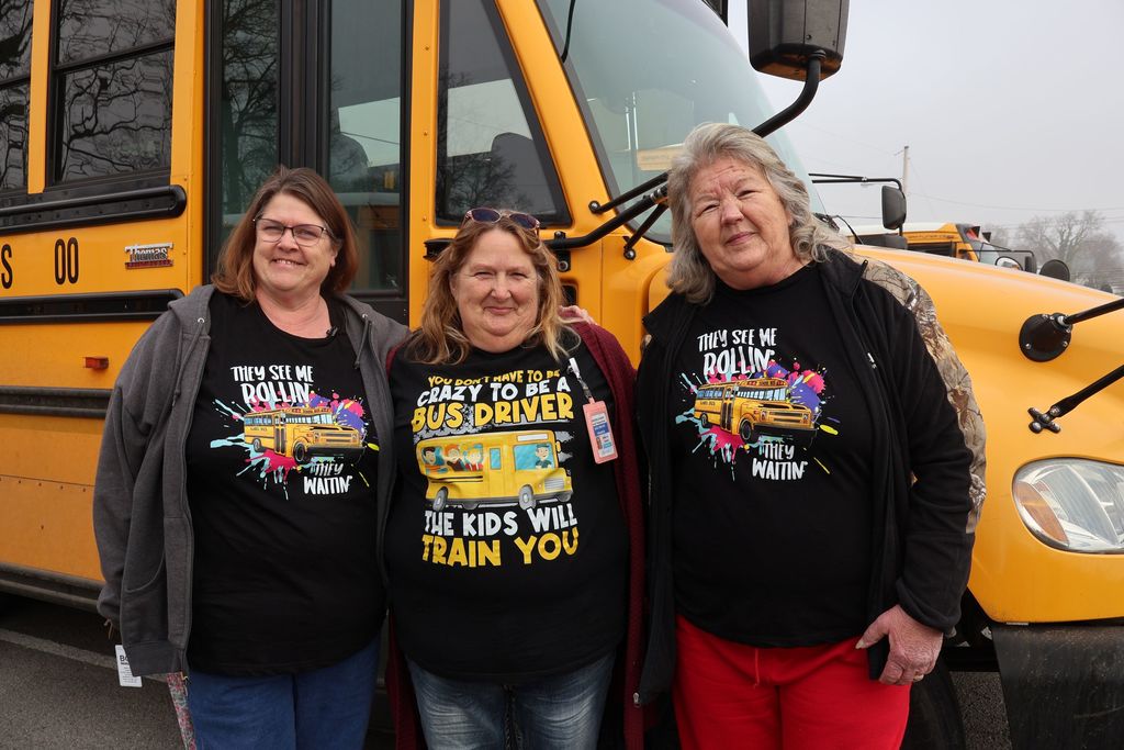 A group photo of three special education bus drivers by a school bus. 