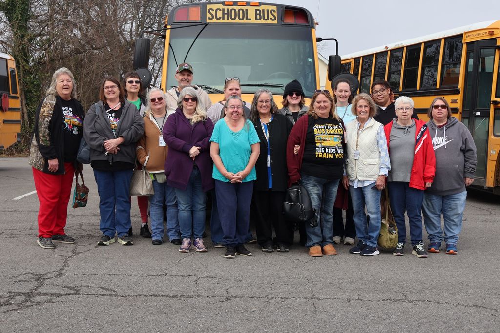 Group photo of the Special Education bus drivers in front of some school buses.