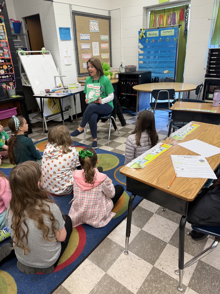 Guest reader reads Horton Hatches the Egg to students sitting on their classroom carpet. 