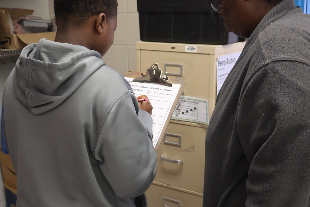 Student writing on a clipboard with parent looking on. 