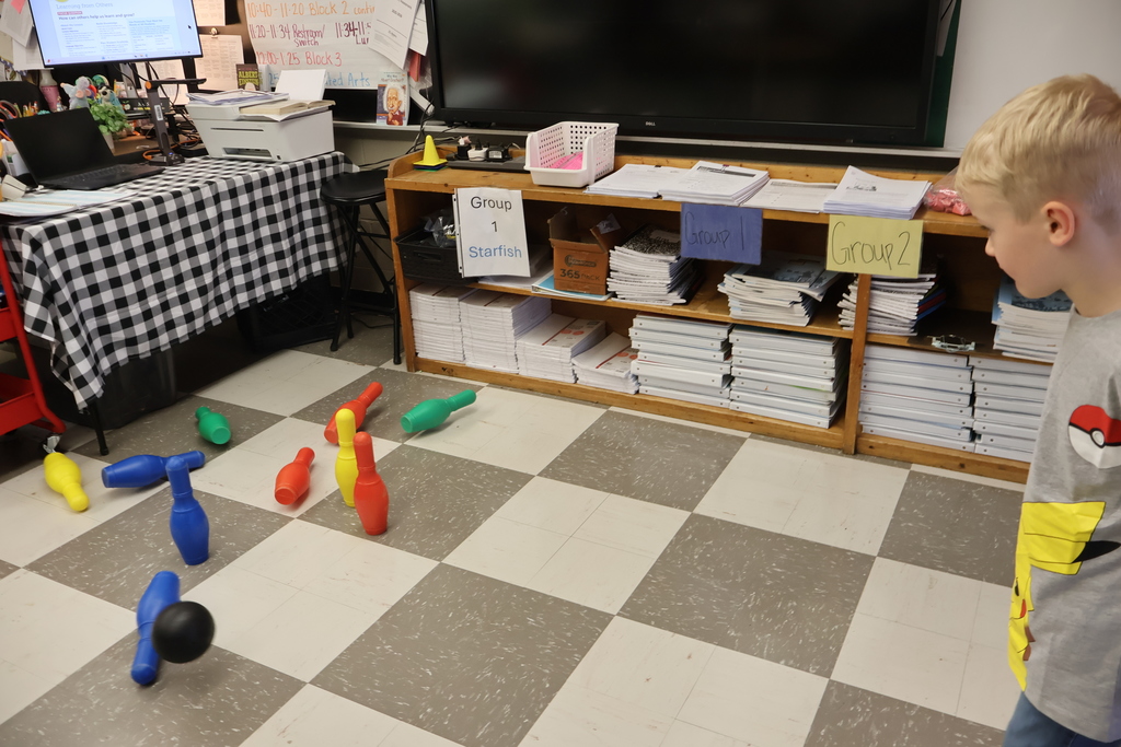 Student playing knocked over bowling pins with ball.