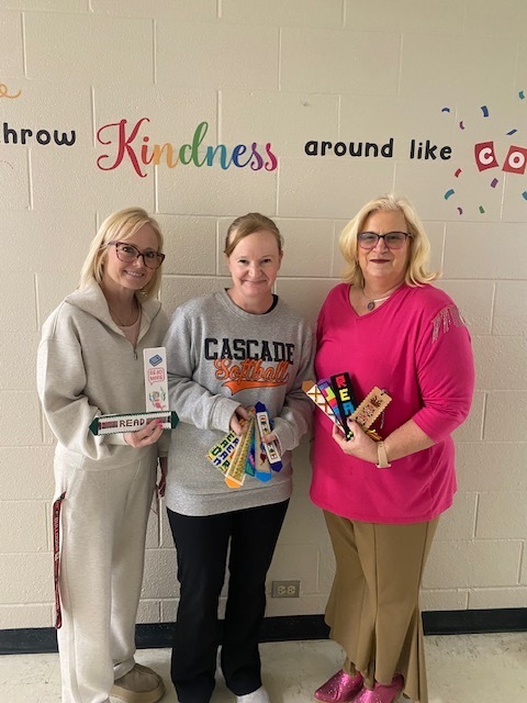 Picture of three people against a wall holding handstitched bookmarks. 
