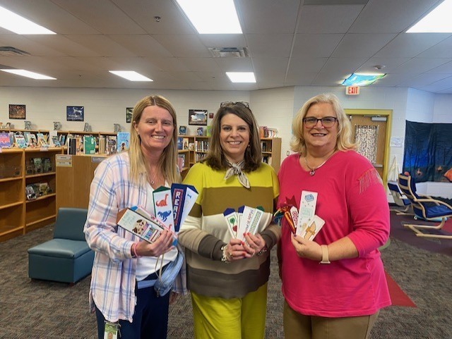 Picture of three people in the library holding handstitched bookmarks. 