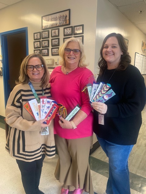 Picture of three people against a wall holding handstitched bookmarks. 