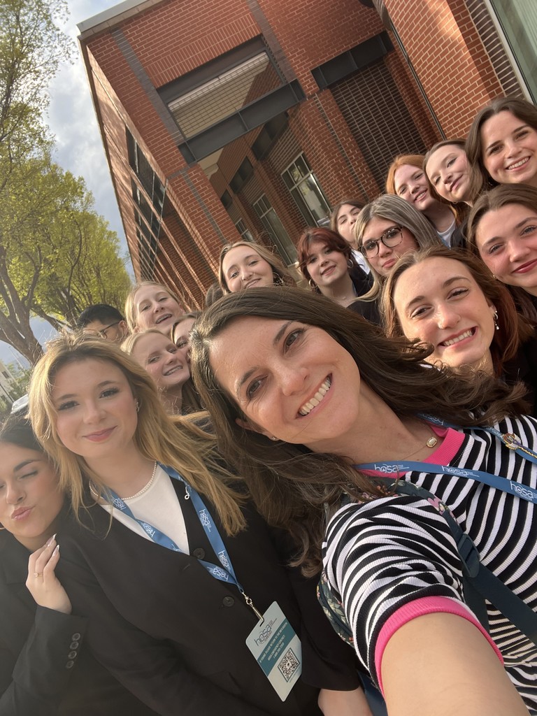 HOSA students along with their instructor pose for a picture outside by a building. 