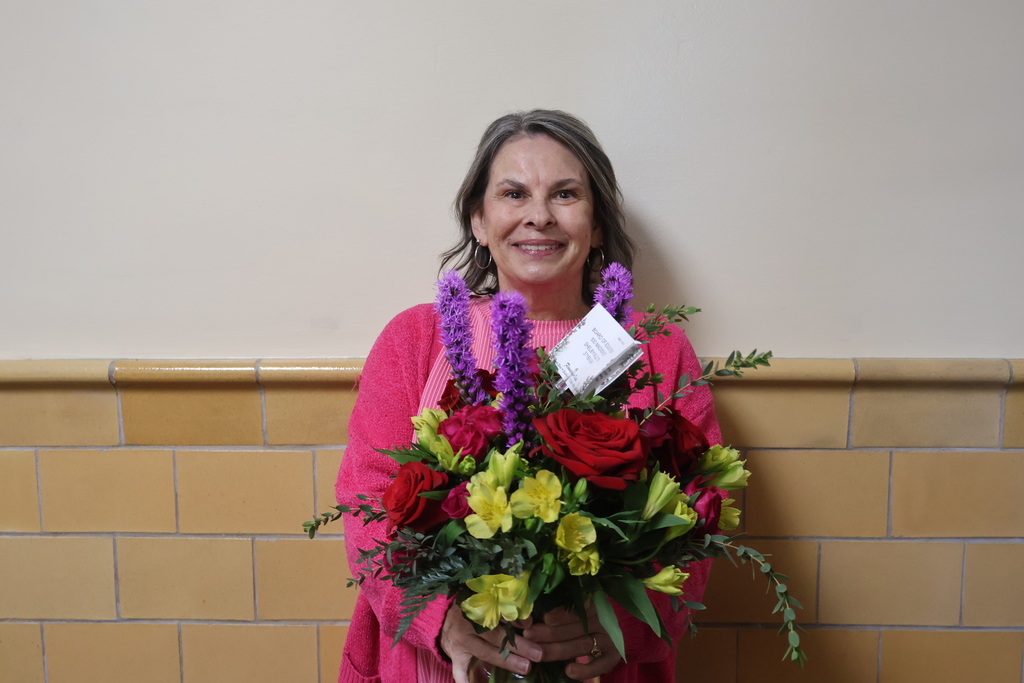 Central Office Support Person of the Year Laurie Brannon stands for a  picture while holding a vase of flowers.
