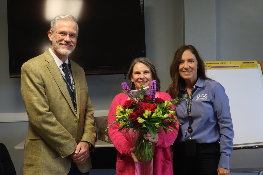 Central Office Support Person of the Year Laurie Brannon stands for a group picture with the Assitant Superintendent and Superintendent while holding flowers. 