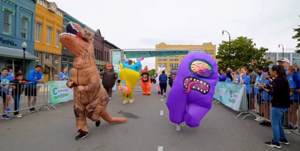 People dressed in inflatable costumes running the CC5K race as other people cheered them on.