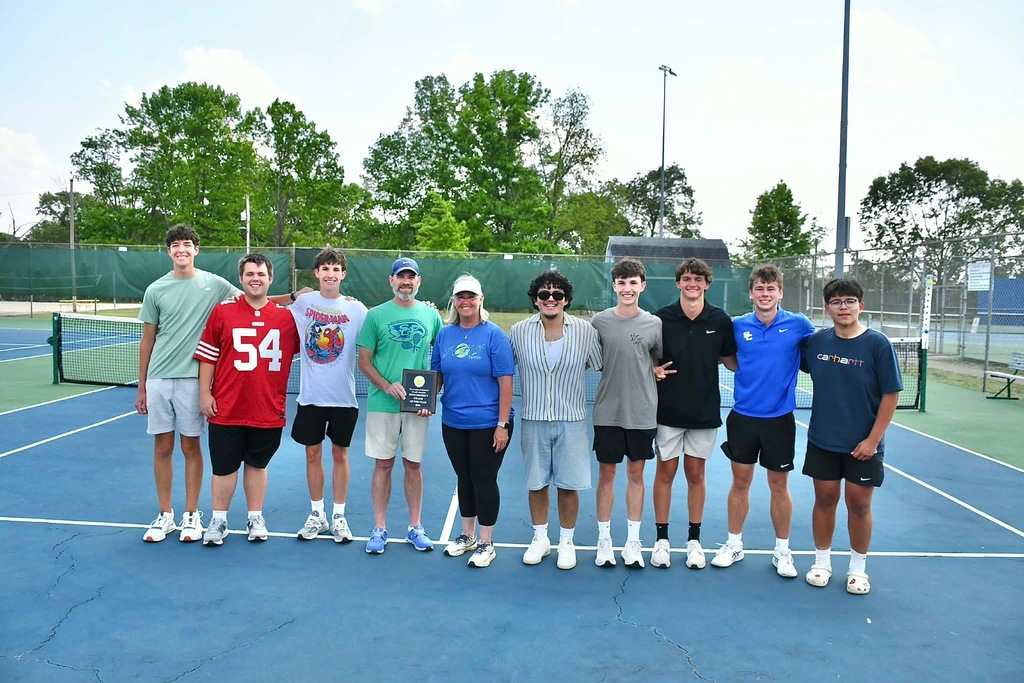 A group of student atheletes, along with their coaches, are standing on the tennis court for a group picture. 