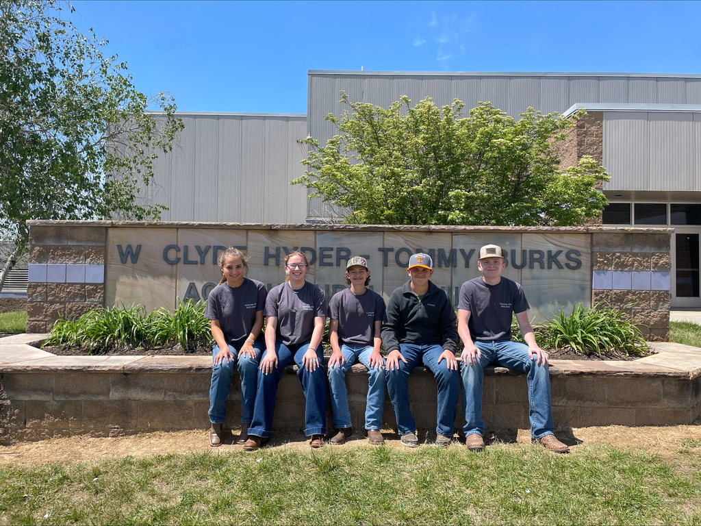A group of FFA students from Cascade High School pose for a picture sitting on a stone wall outside of a building. 