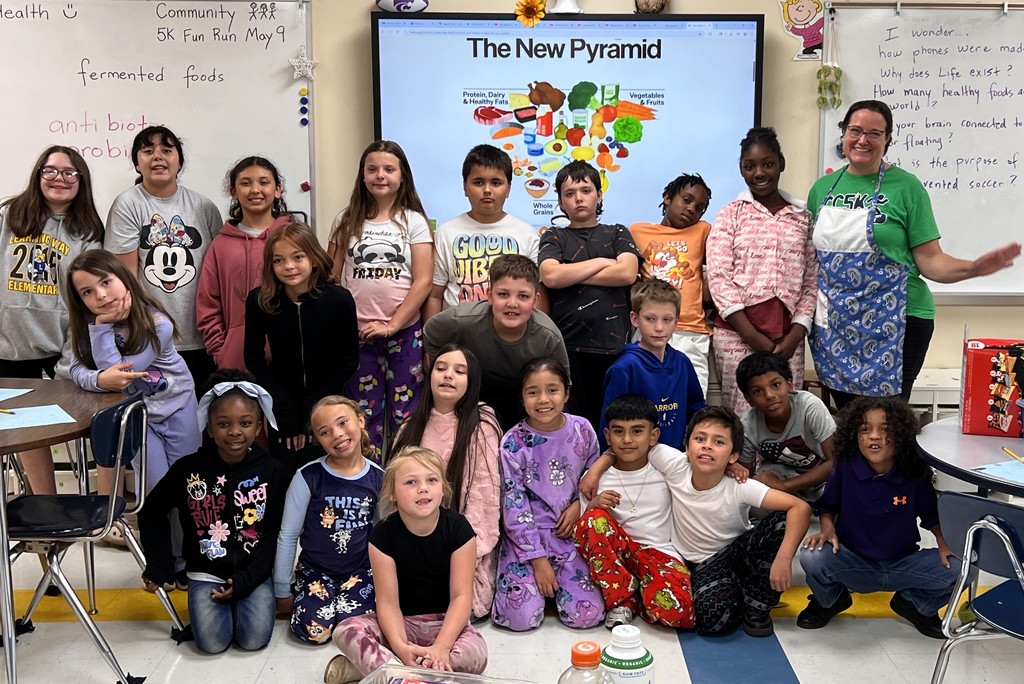 A group photo of students and their teacher in front of The New Pyramid Graphic.