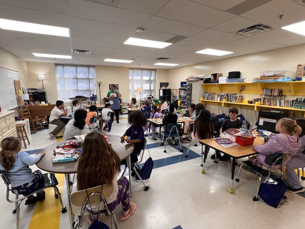 Students are sitting at tables listening to the teacher speak. 