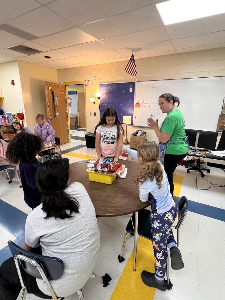 Students are sitting at tables listening to the teacher speak. 