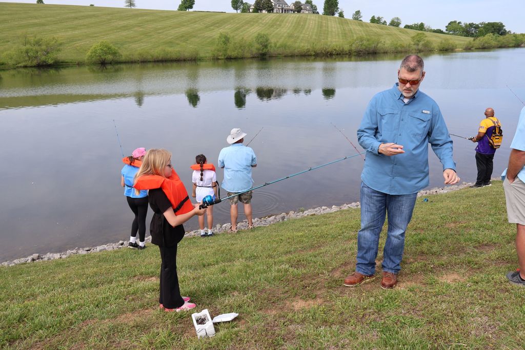 A member of the school board helps a student with her fishing pole.