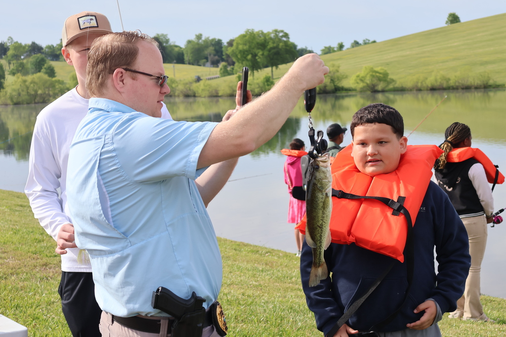 A student and several adults help him weigh the fish that he caught. 