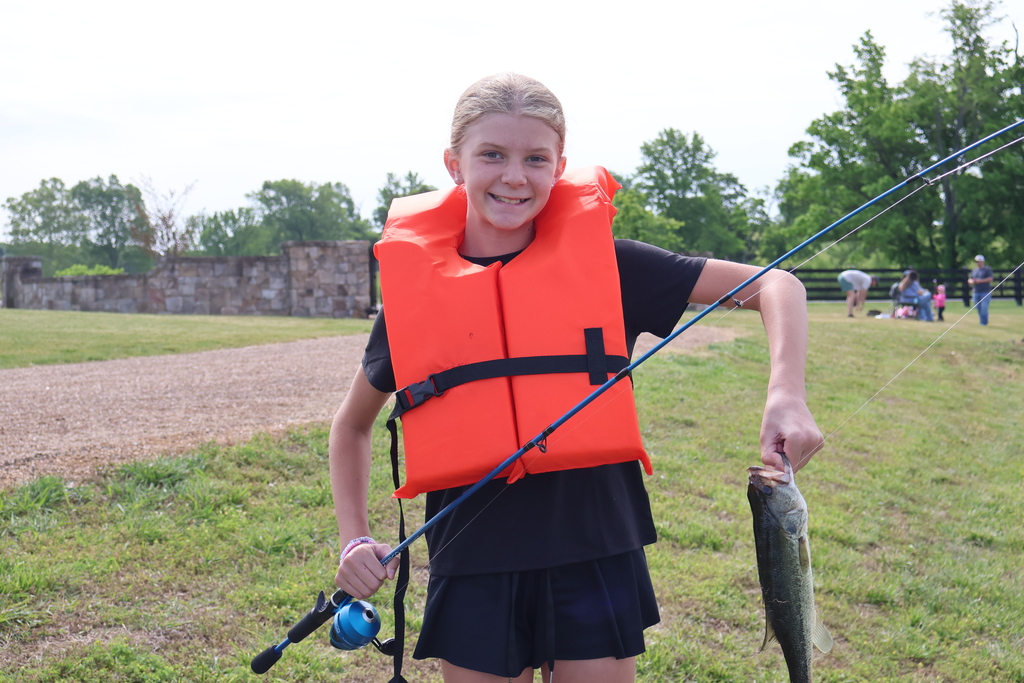 Student holding fishing pole and fish that she caught.