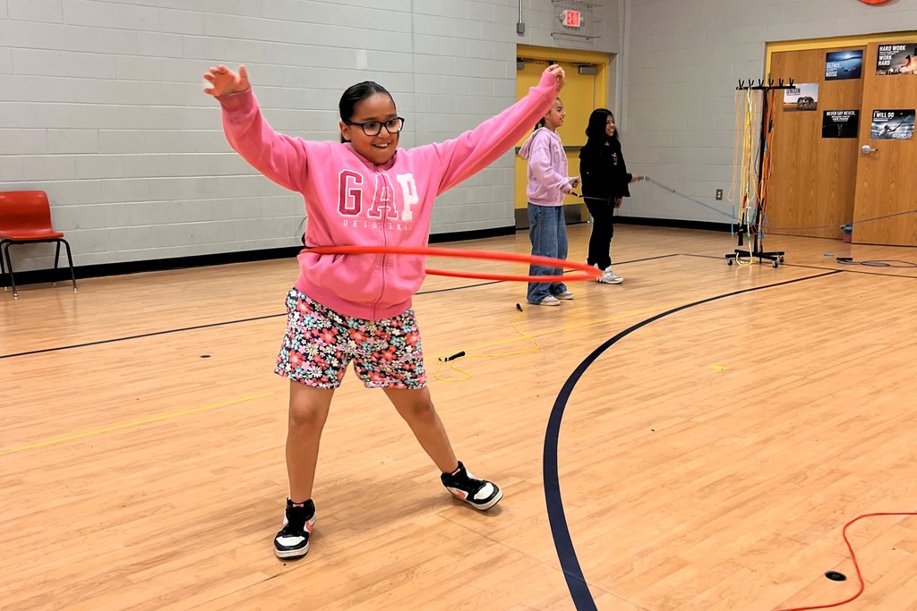 Student is using a hula hoop in the gym. 
