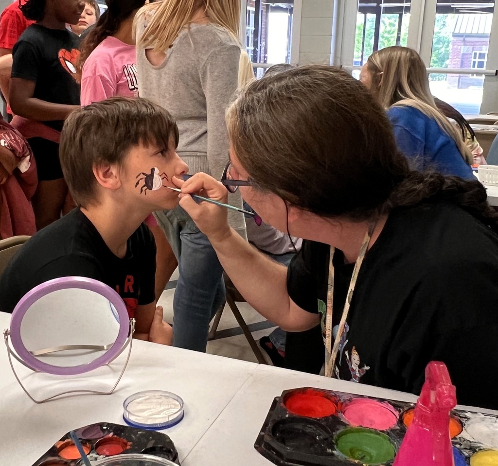 Student is getting a spider on his face with face paint. 