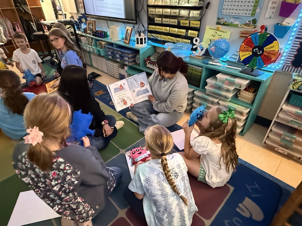Elementary students are reading with high school students on the carpet.