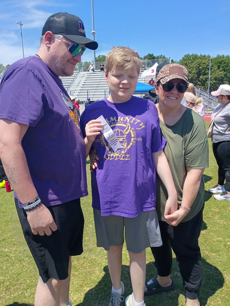 A student and his parents pose fora  picture while he is holding the ribbon that he won.