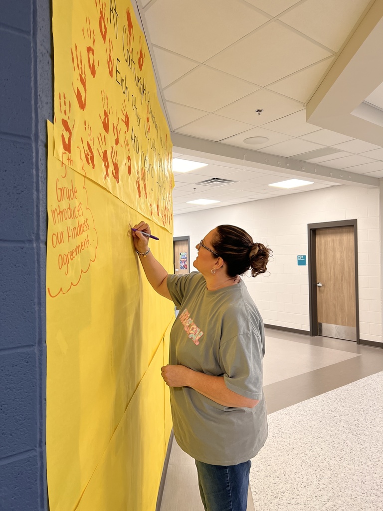 The principal is writing a message on the banner students made.