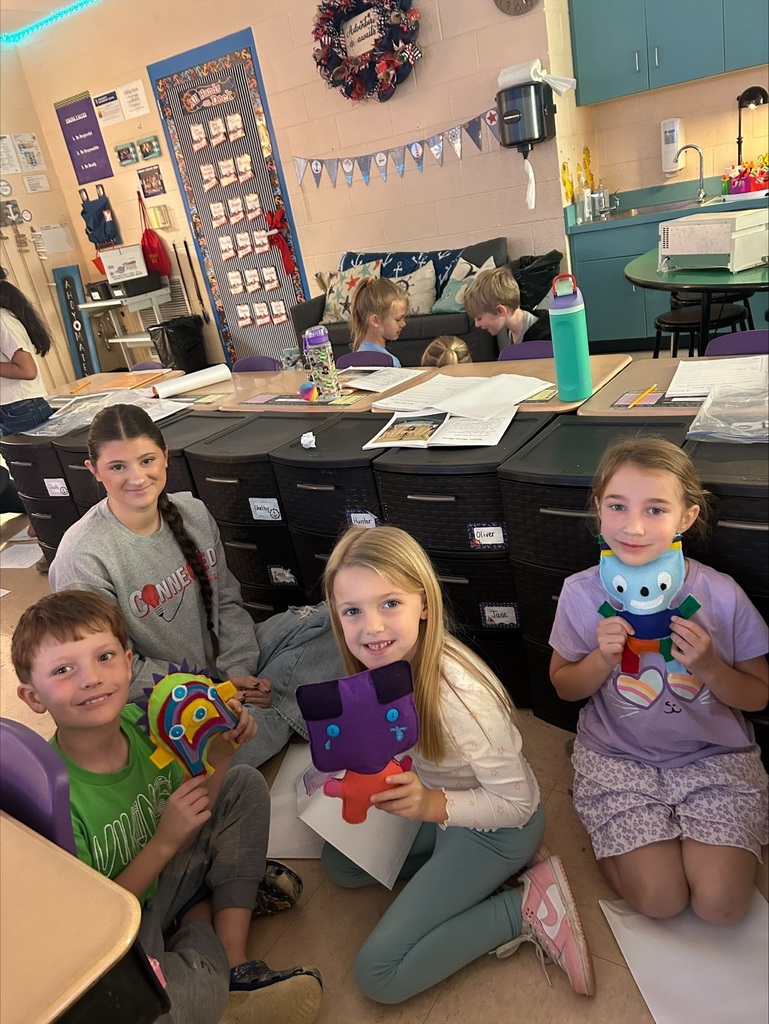 Three elementary students are holding up the friendly monsters the high school students made. 