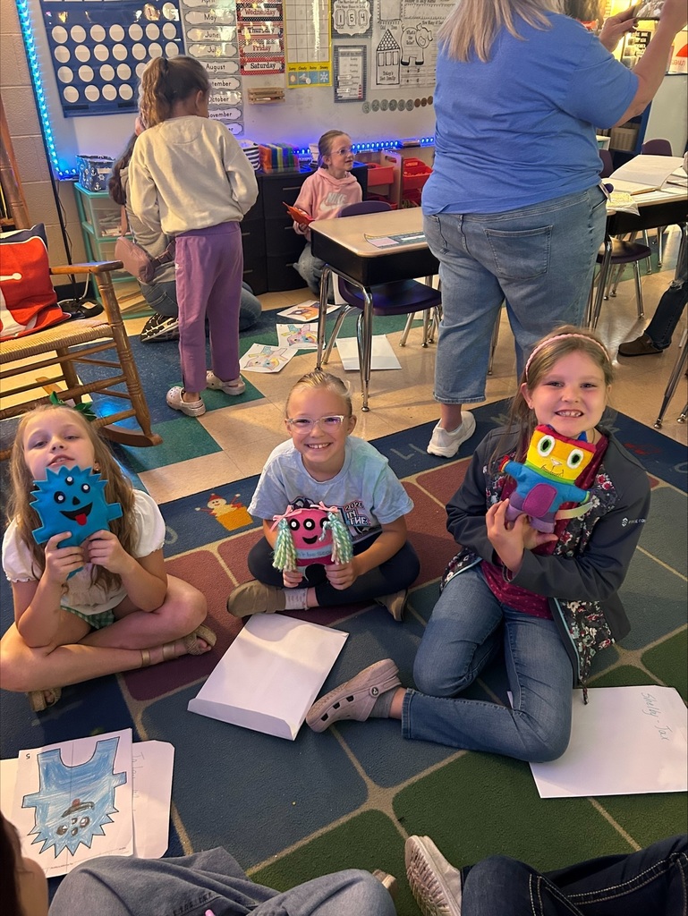 Three elementary students are holding up the friendly monsters the high school students made. 