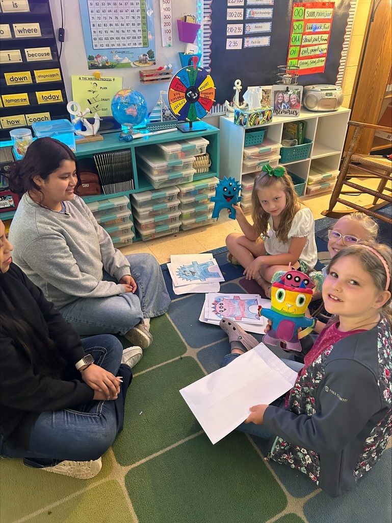 Three elementary students are holding up the friendly monsters the high school students made. 