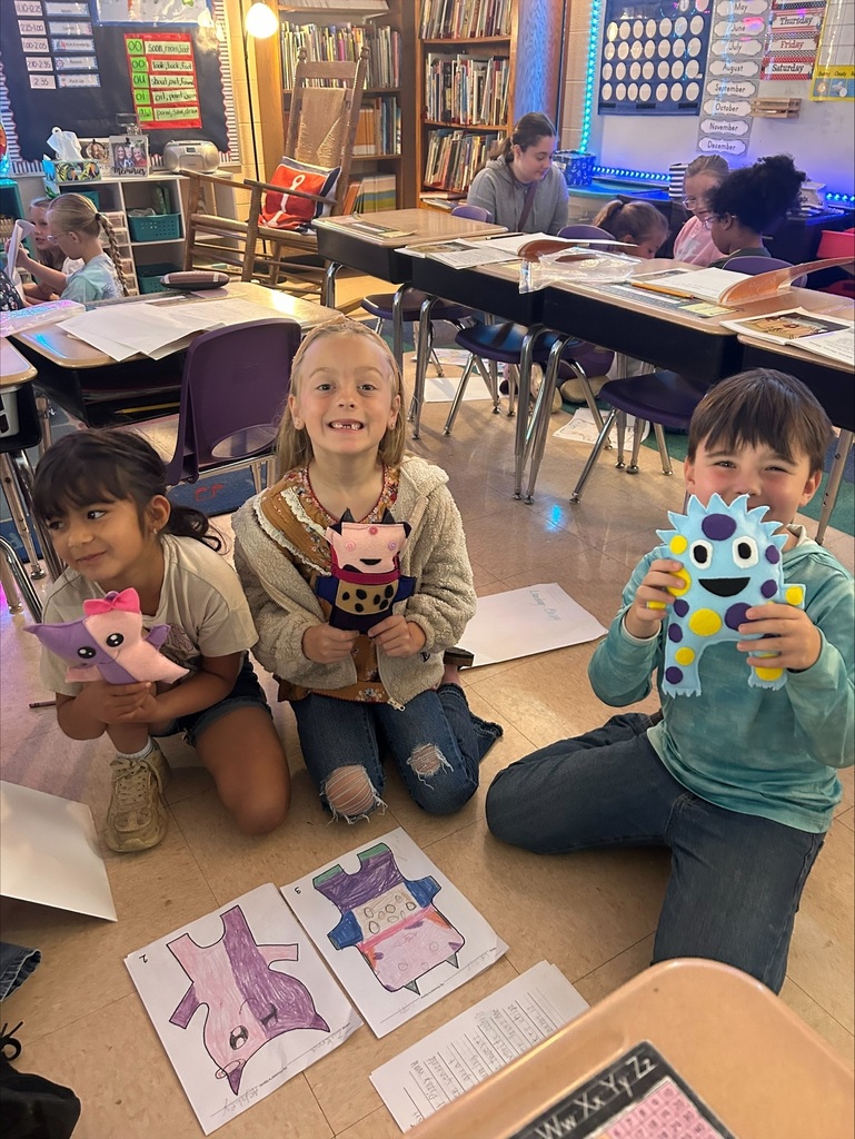 Three elementary students are holding up the friendly monsters the high school students made. 
