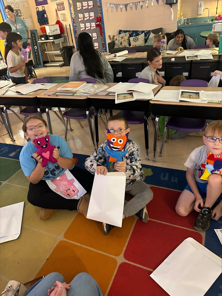 Three elementary students are holding up the friendly monsters the high school students made. 