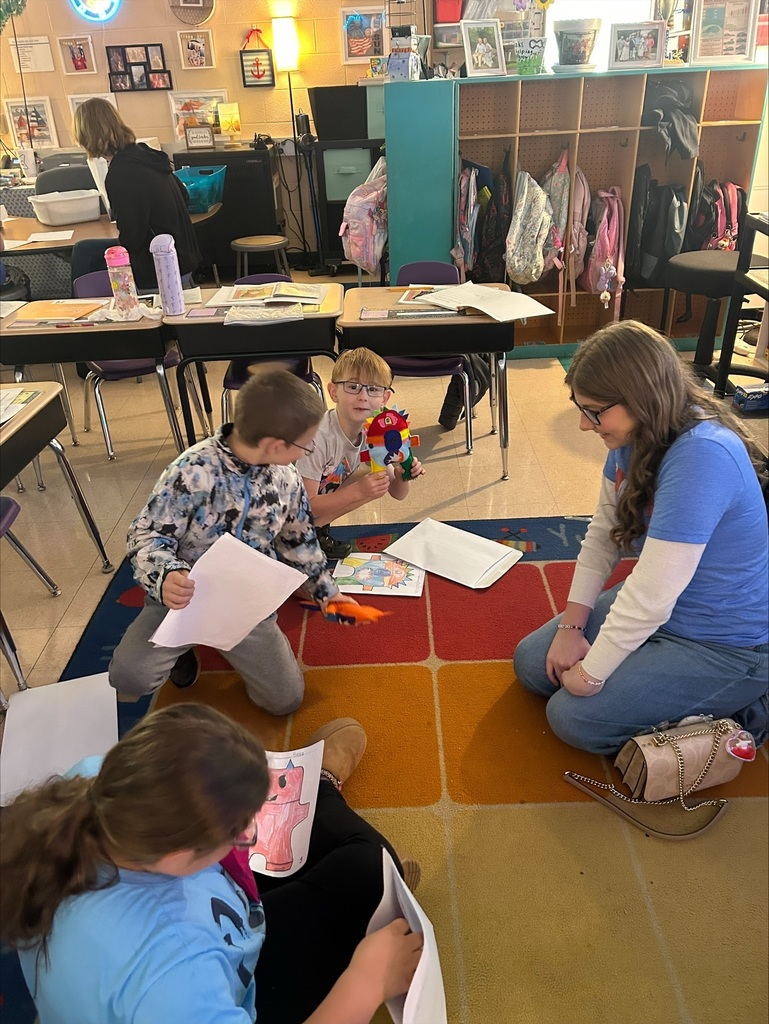 Three elementary students are holding up the friendly monsters the high school students made. 