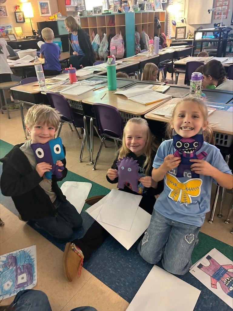 Three elementary students are holding up the friendly monsters the high school students made. 