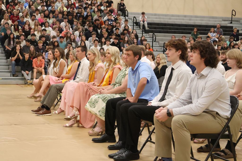 The top ten seniors from Cascade High School are sitting down in chairs on the gym floor.