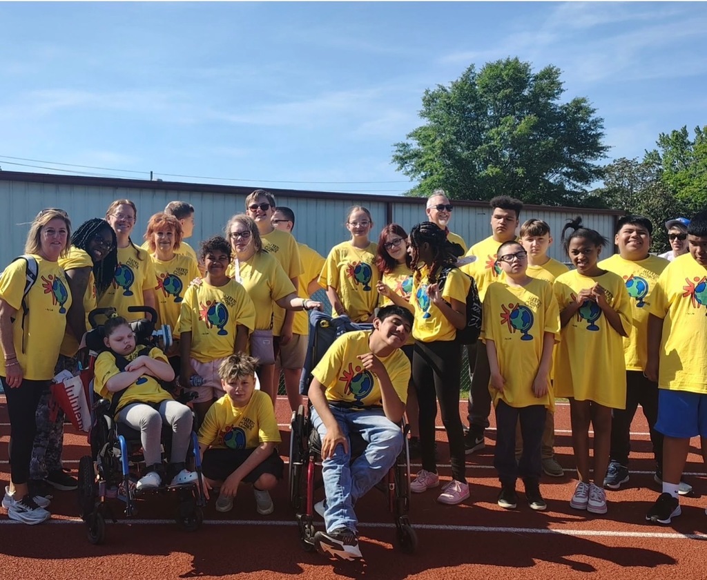Students, along with their teacher and aides, all pose for a group picture on the track wearing yellow shirts. 