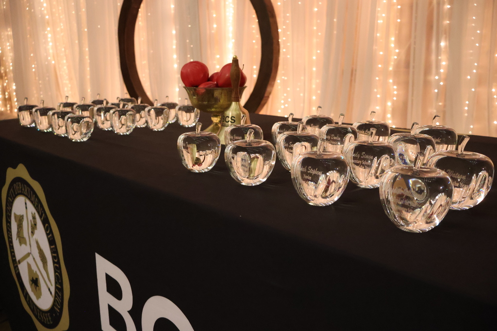 Glass apple awards on a black table with lights in behind it. 