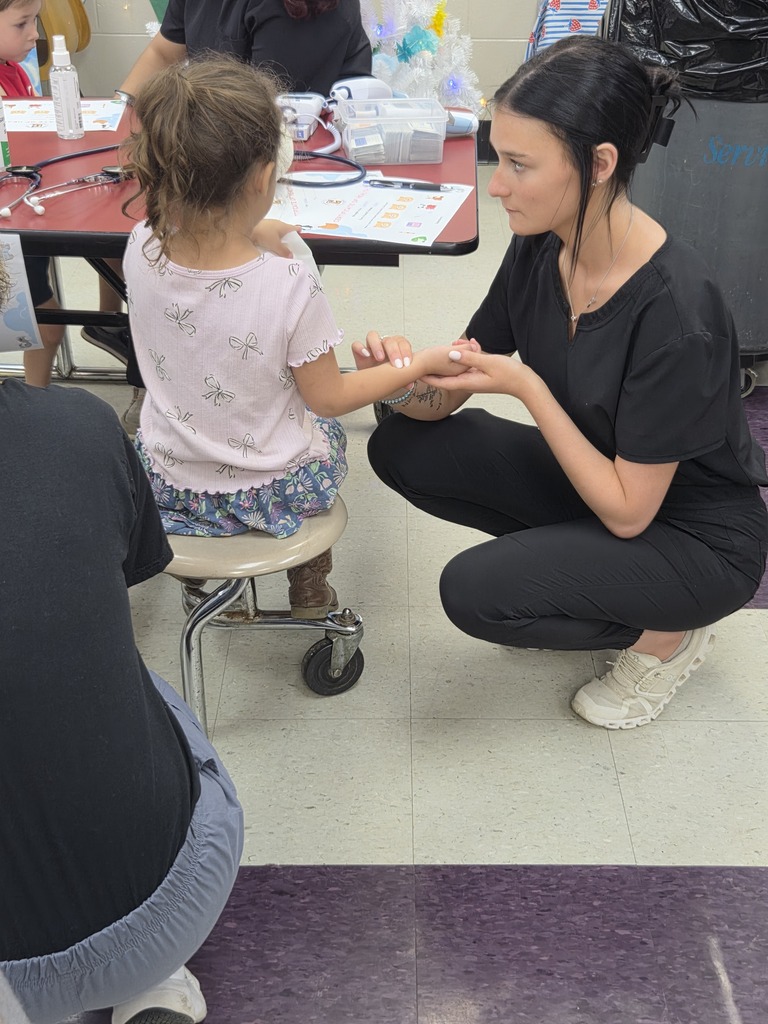 A Pre-K student is having her pulse checked by a high school student.