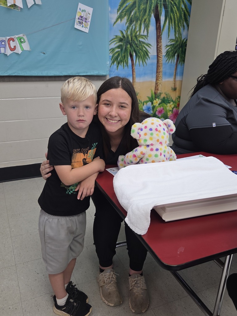 A Pre-K student poses for a picture with a high school student and their stuffed animal. 