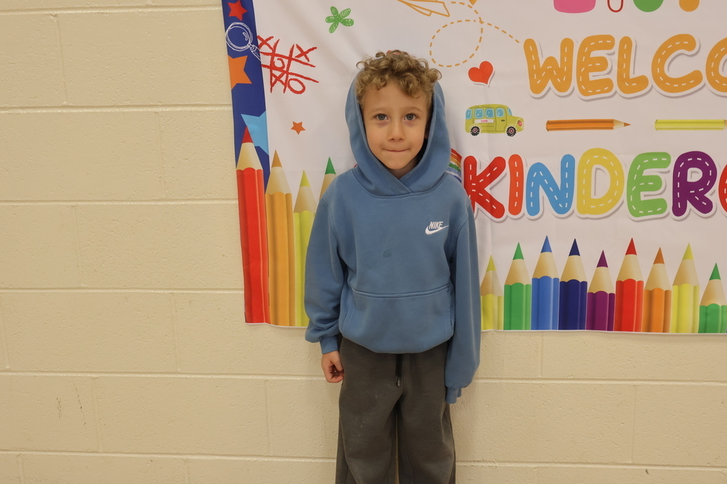 A boy is standing by a wall in front of a welcome sign for kindergarten.