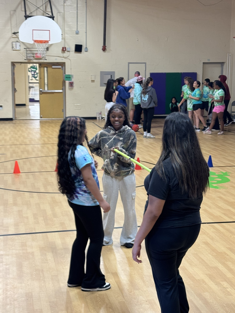 One elementary student is participating in a llimbo activity as two TAP students help hold the pole. 