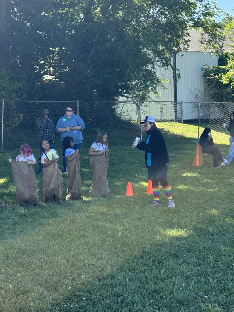 Four elementary students participate in a sack race as TAP students help with activities. 