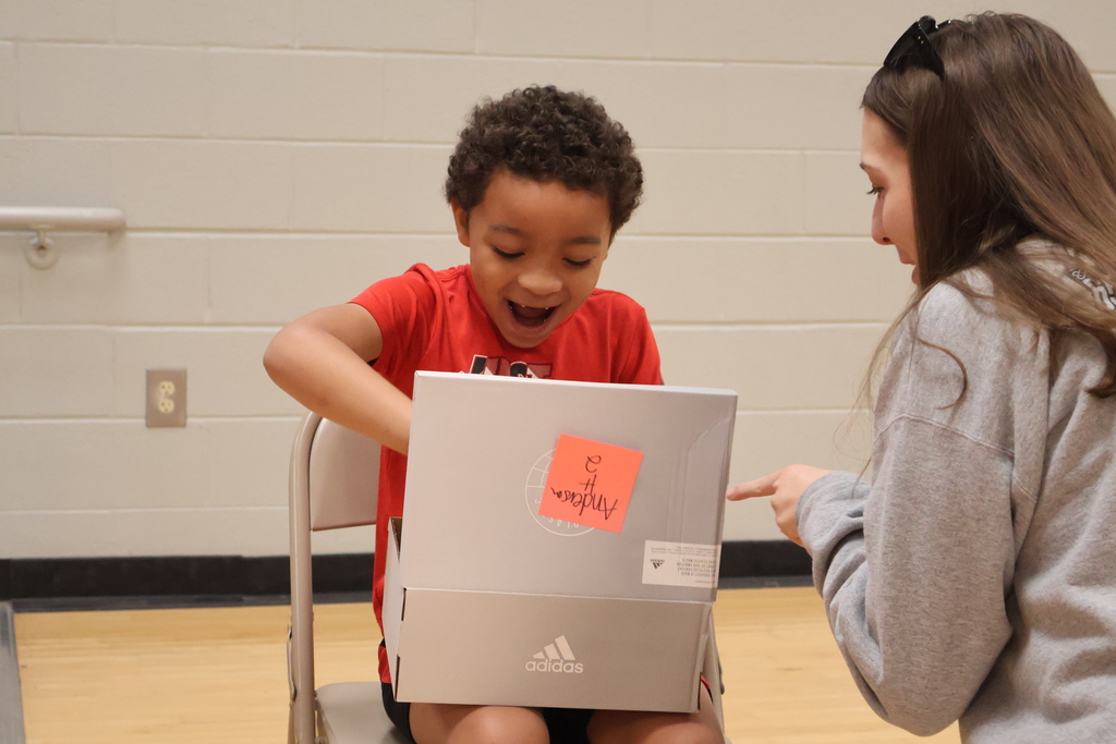 A student, sitting in a chair,  is excited about the new shoes he has received.