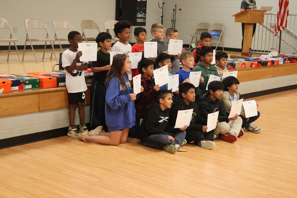 Students pose for a group picture in the gym with the certificates that they earned for the miles they ran. 