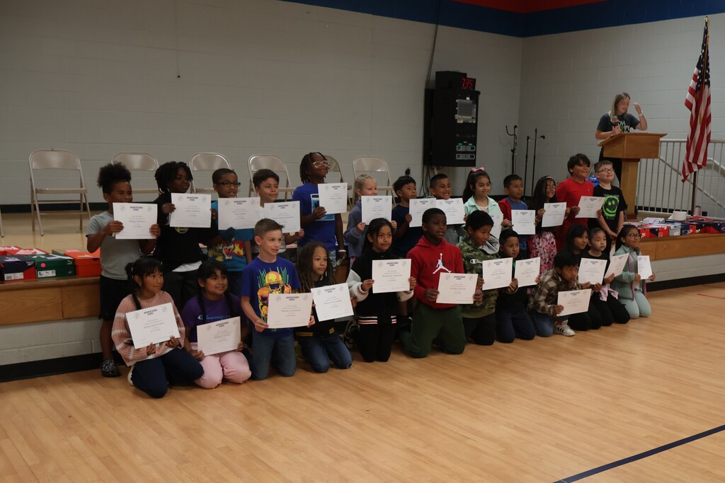 Students pose for a group picture in the gym with the certificates that they earned for the miles they ran. 
